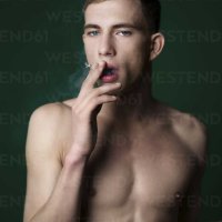 Portrait of self-confident nude young man smoking a cigarette in studio stock photo
